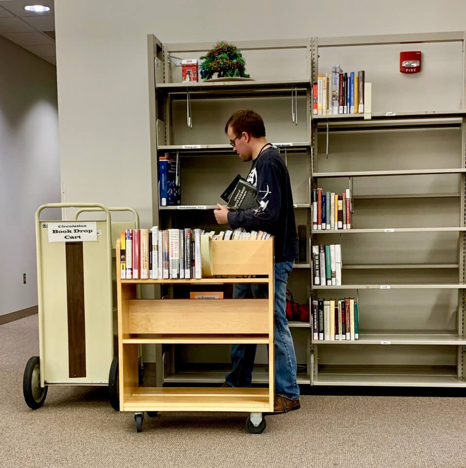 Student stocking books on a library shelf